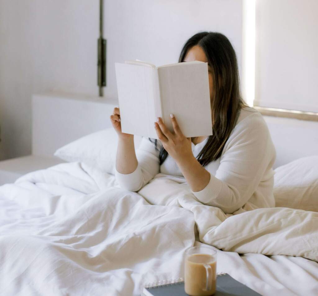  A woman finding solace in a book, seeking ways to escape a slump, cozily reading on her bed.