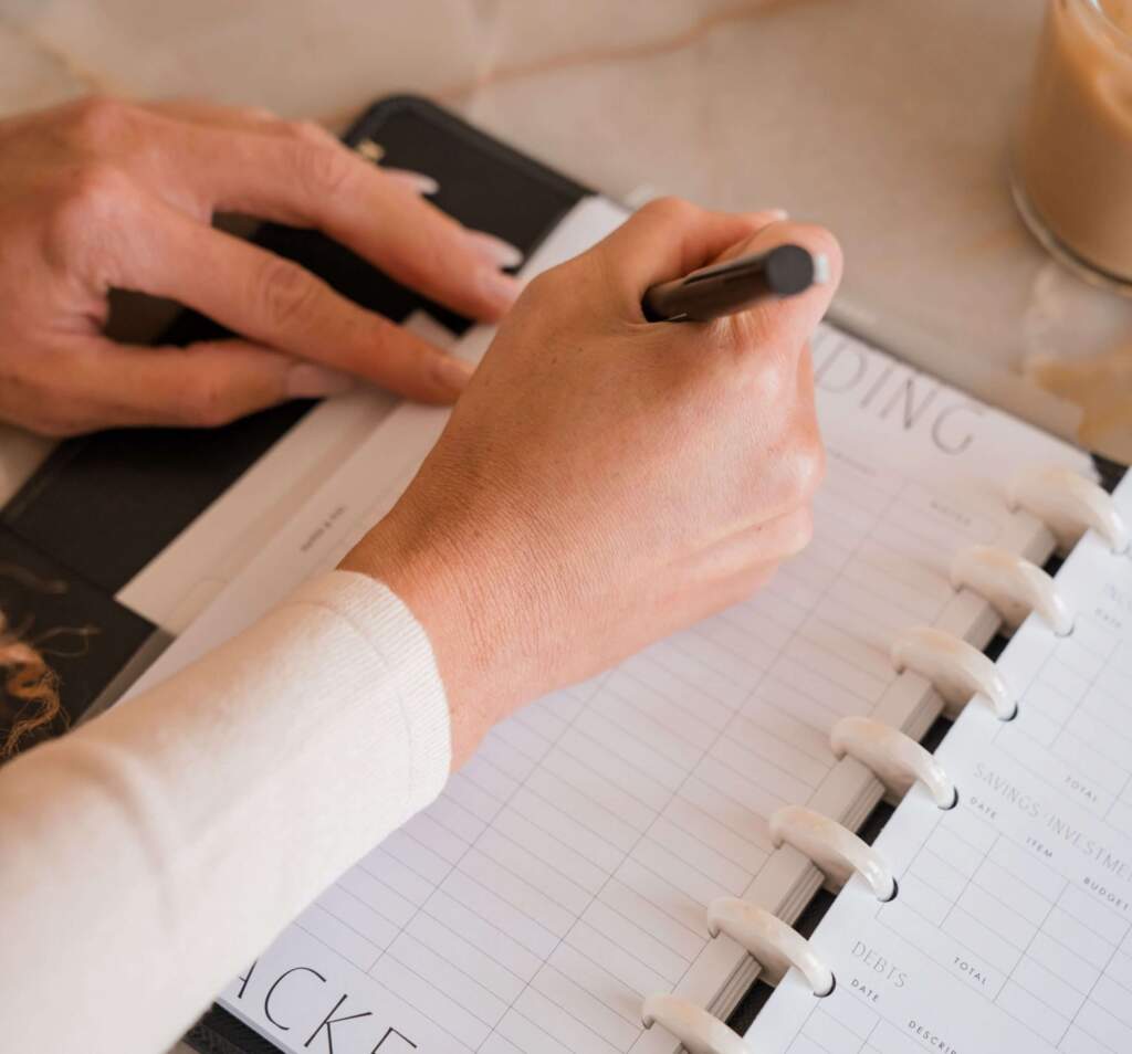 A woman's hand writing on a journal, organizing tasks and goals, seeking ways to overcome a slump.


